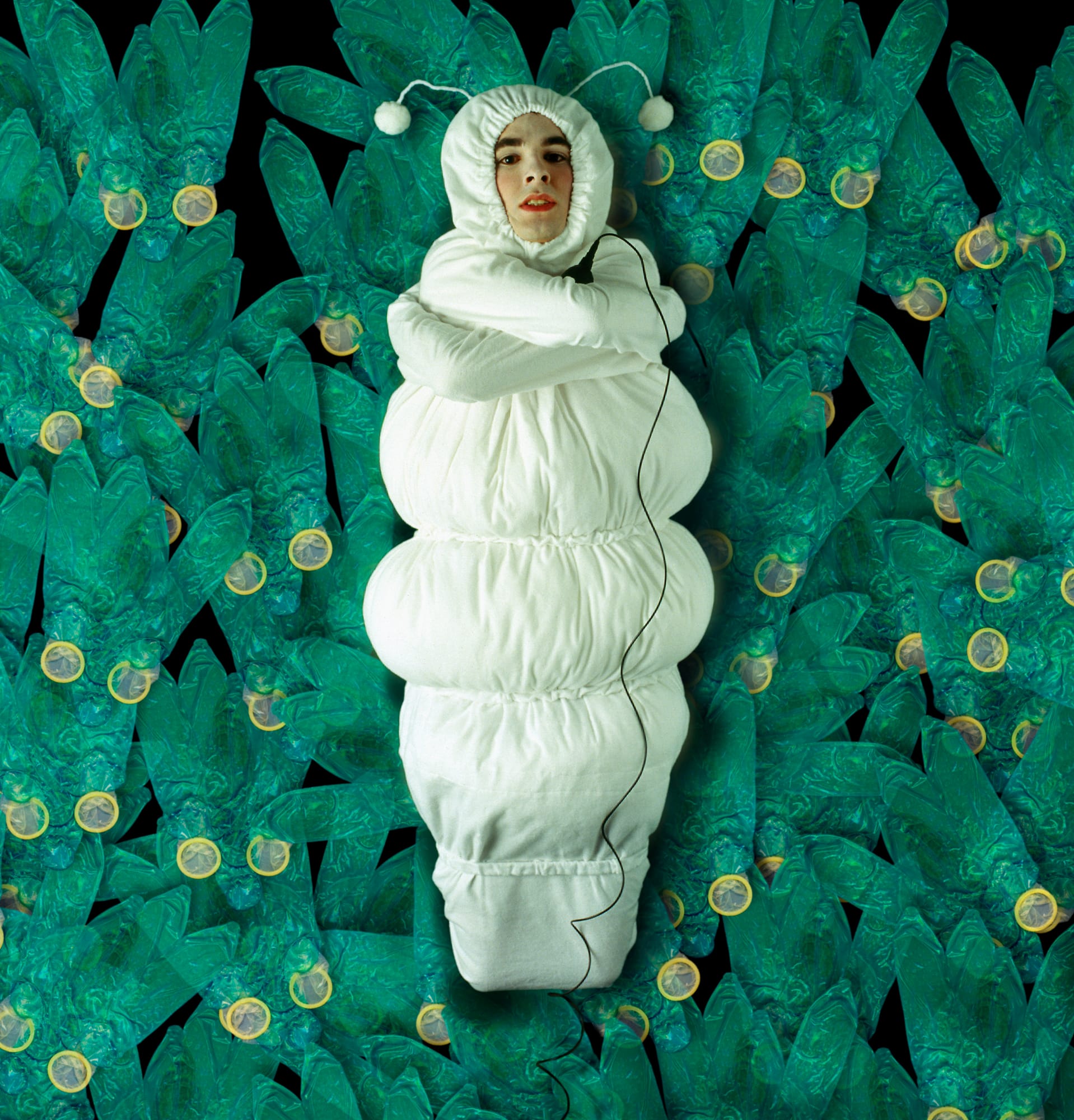 Self-portrait as an infant curled in a white padded suit over a bed of turquoise glowing coins.