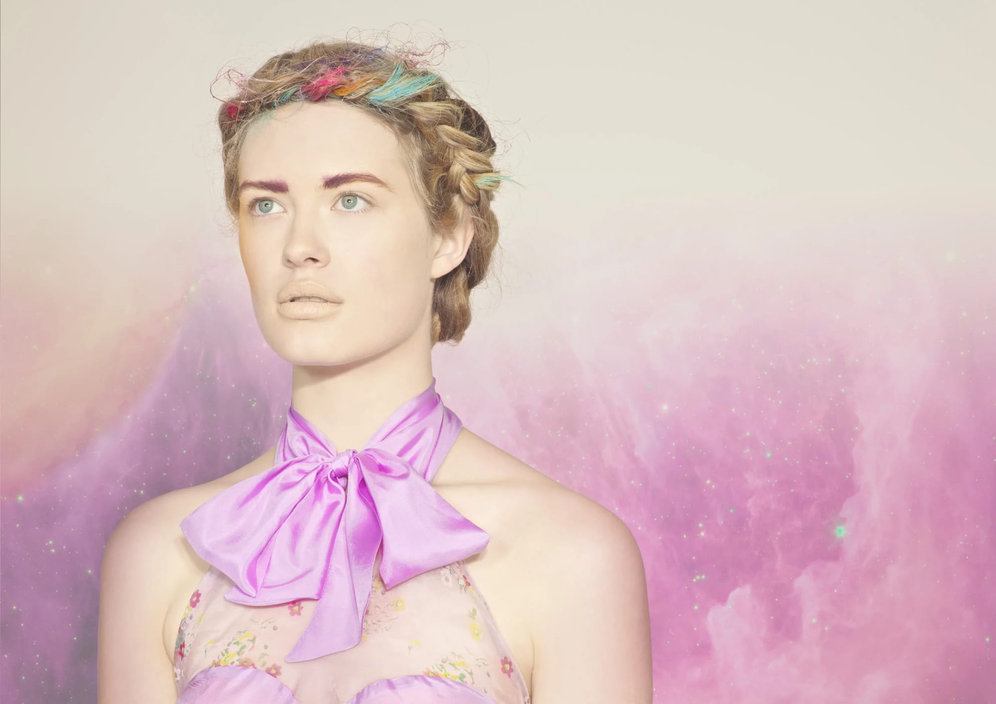 A woman with pastel-coloured hair and a purple satin bowtie, standing against a dreamy pink and purple background with sparkles.