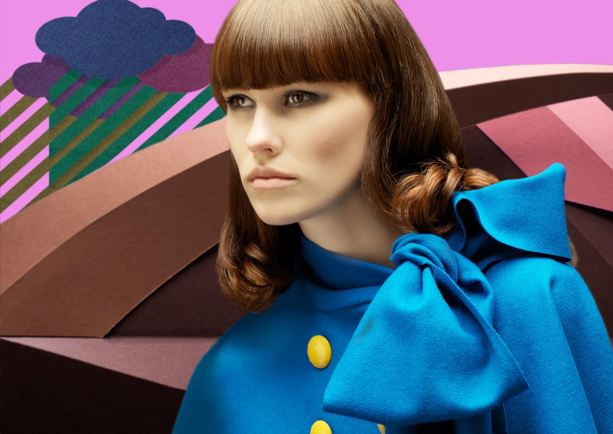 A woman with brown hair and a fringe wearing a bright blue cape with a large bow and yellow buttons, in front of a colourful abstract patterned background.