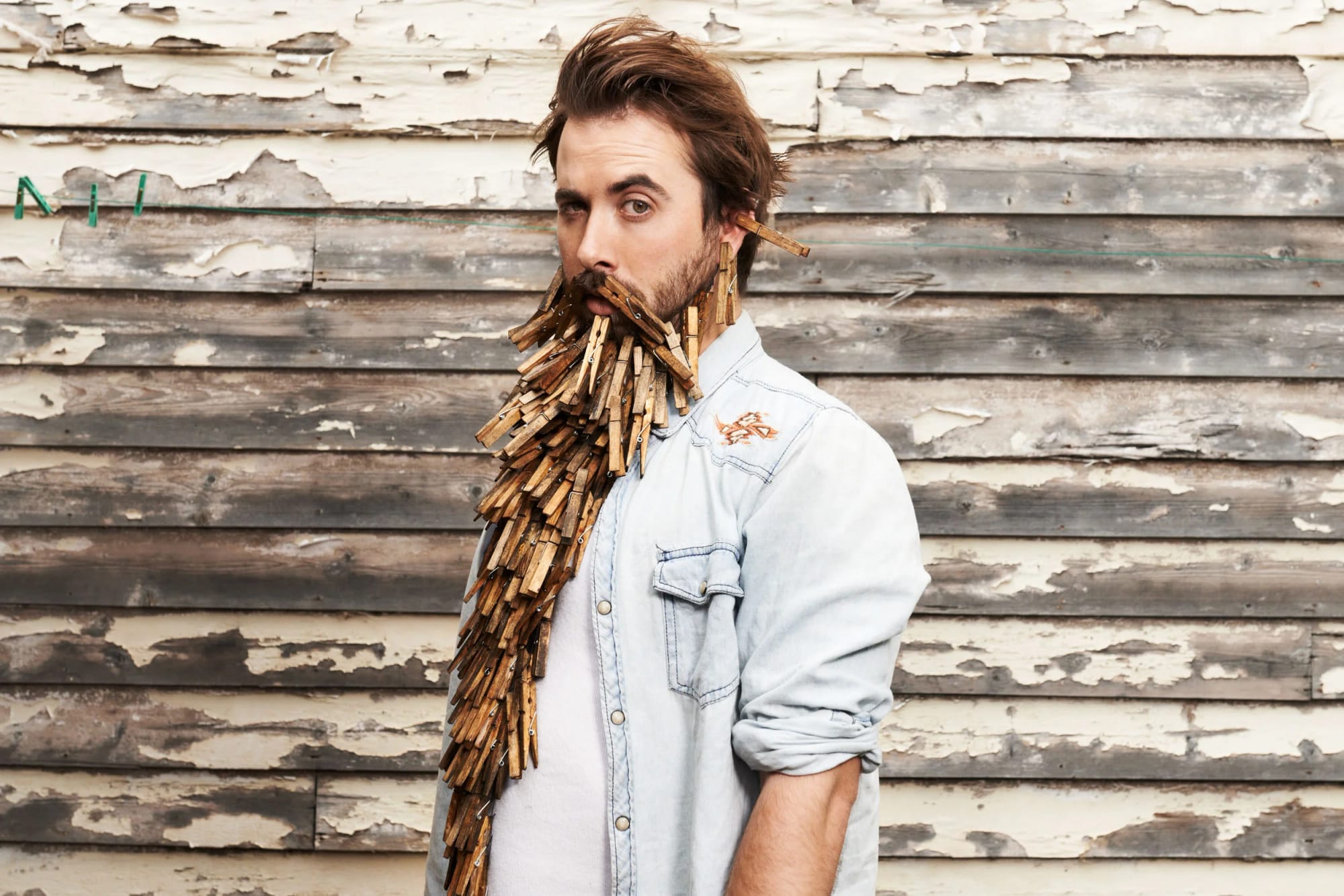 Carlton United Brewing key visual: a man with a beard and brown hair standing in front of a weathered wooden wall, wearing a light denim jacket, with clothespins attached to his beard.