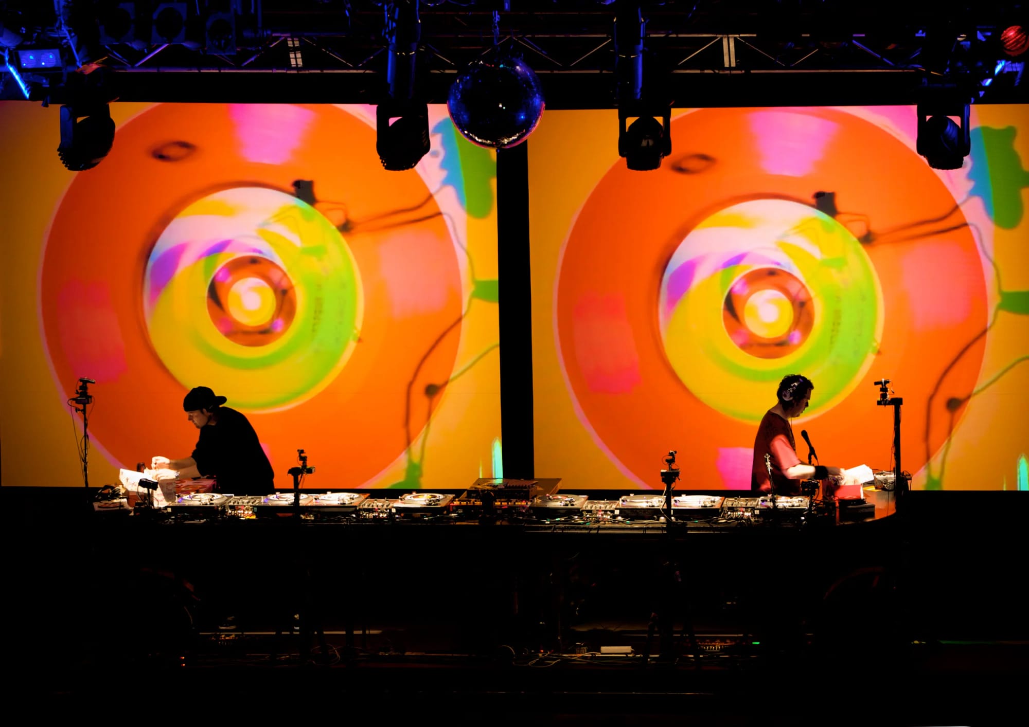 DJ Shadow and Cut Chemist performing on stage with large digital screens behind them displaying swirling colourful abstract patterns.