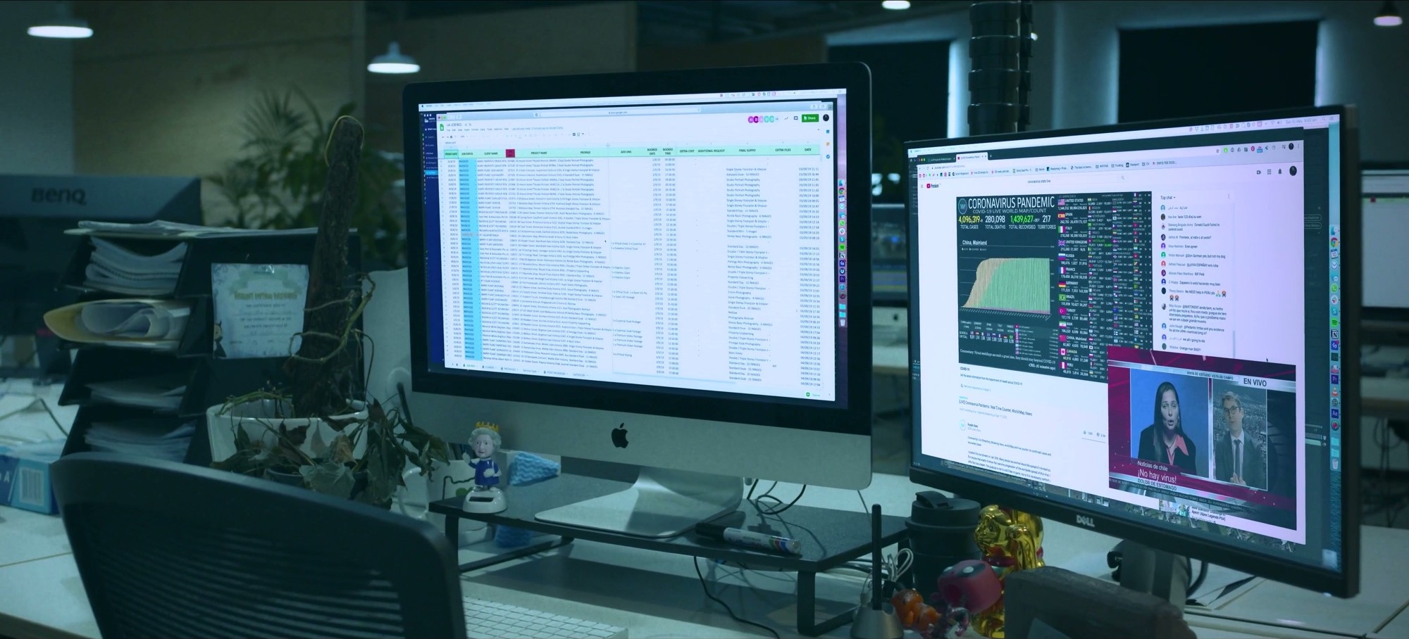 Two computer monitors on an office desk, one showing a spreadsheet and the other a news report and pandemic statistics.