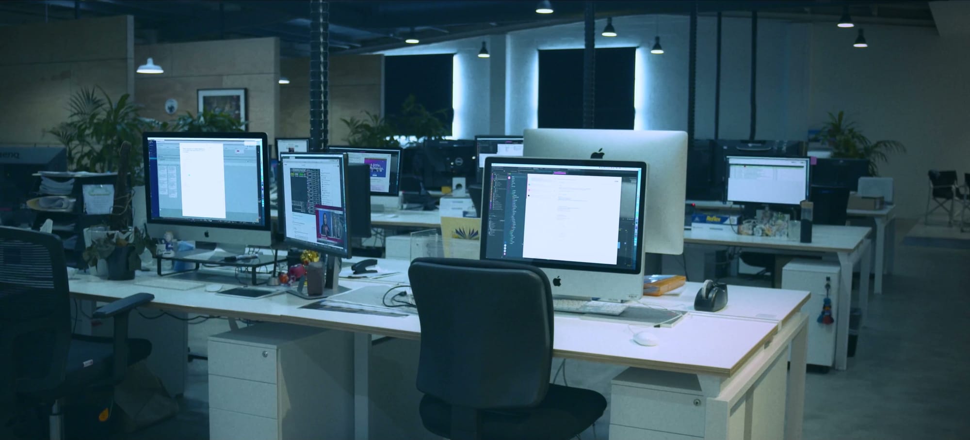 An emptied open-plan office, rows of desktop computers still switched on and every chair pushed back