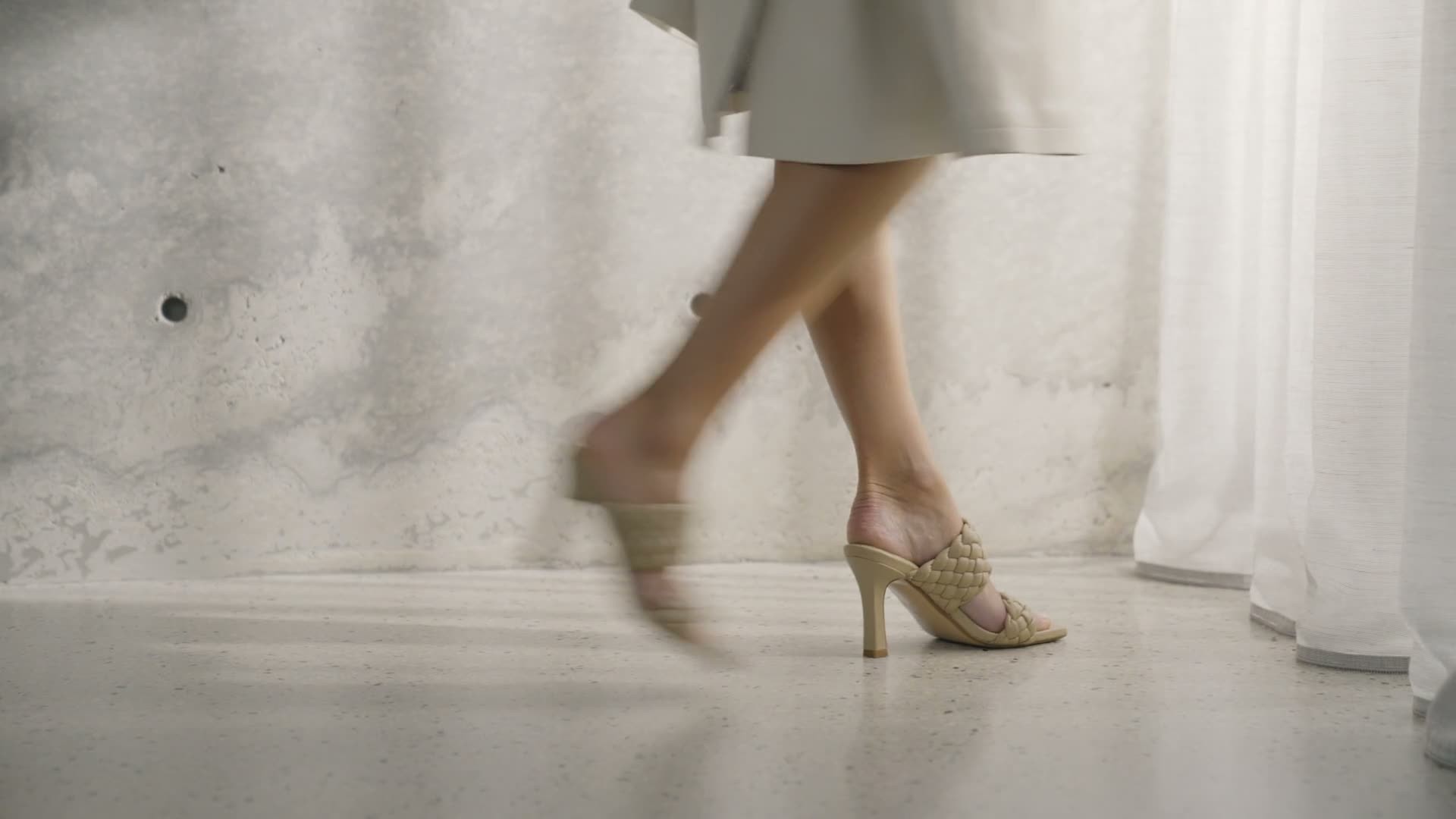 A pair of pale yellow heeled sandals stepping across a sunlit floor beside sheer curtains.