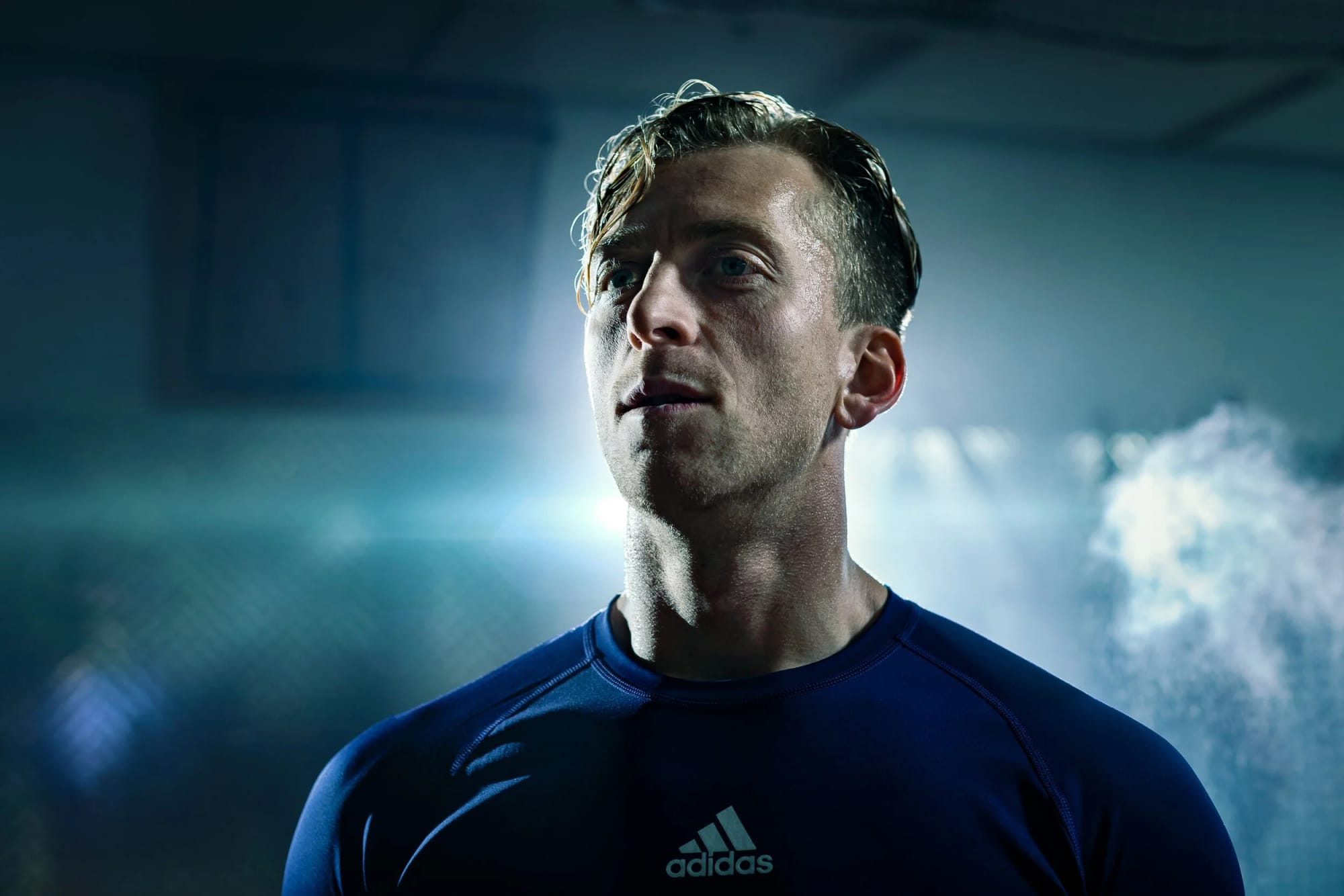 A Melbourne Victory player in a navy training top, lit from behind through smoke, catching his breath