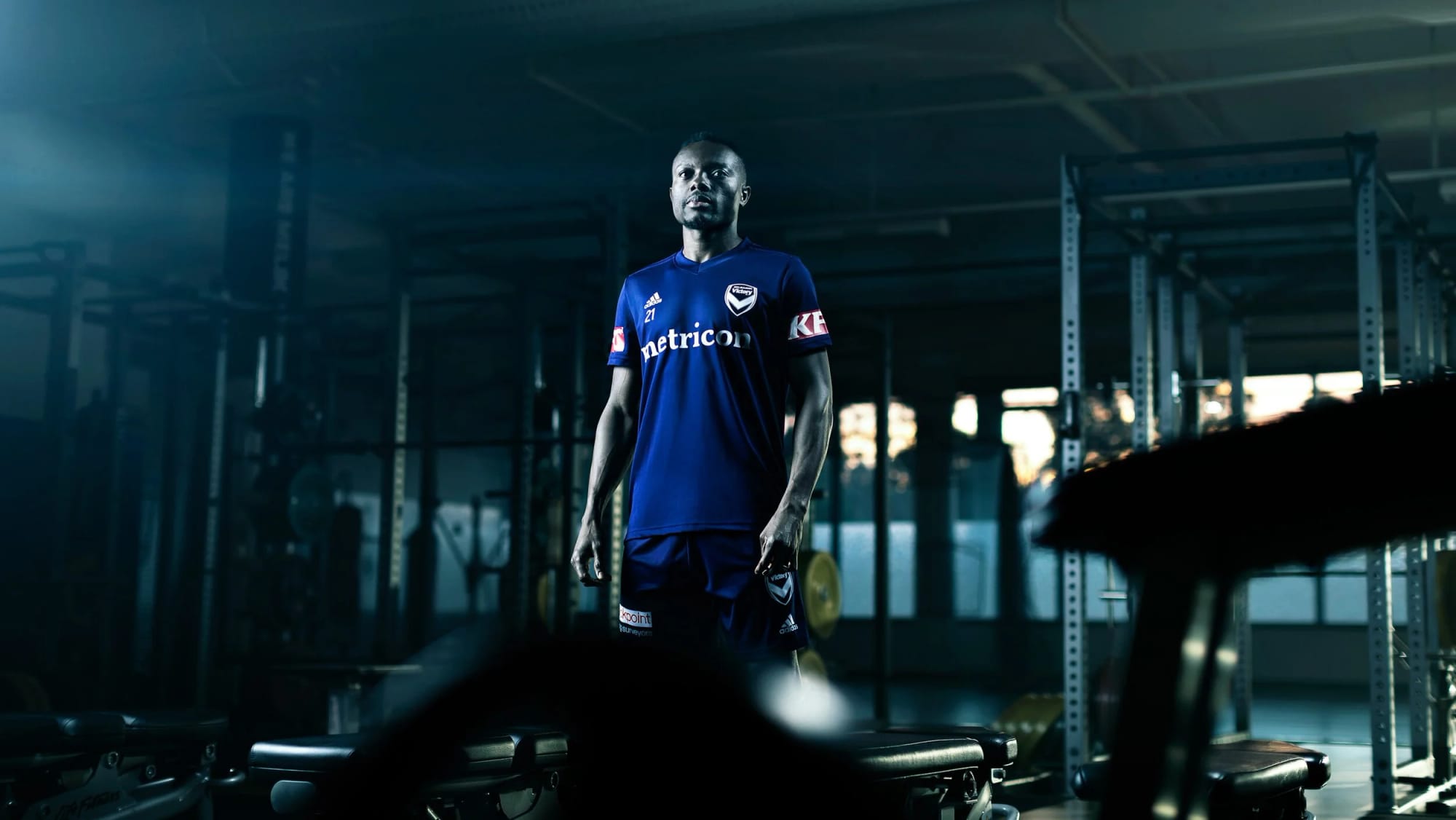 A player standing alone in a dim weights room, the racks running away behind him