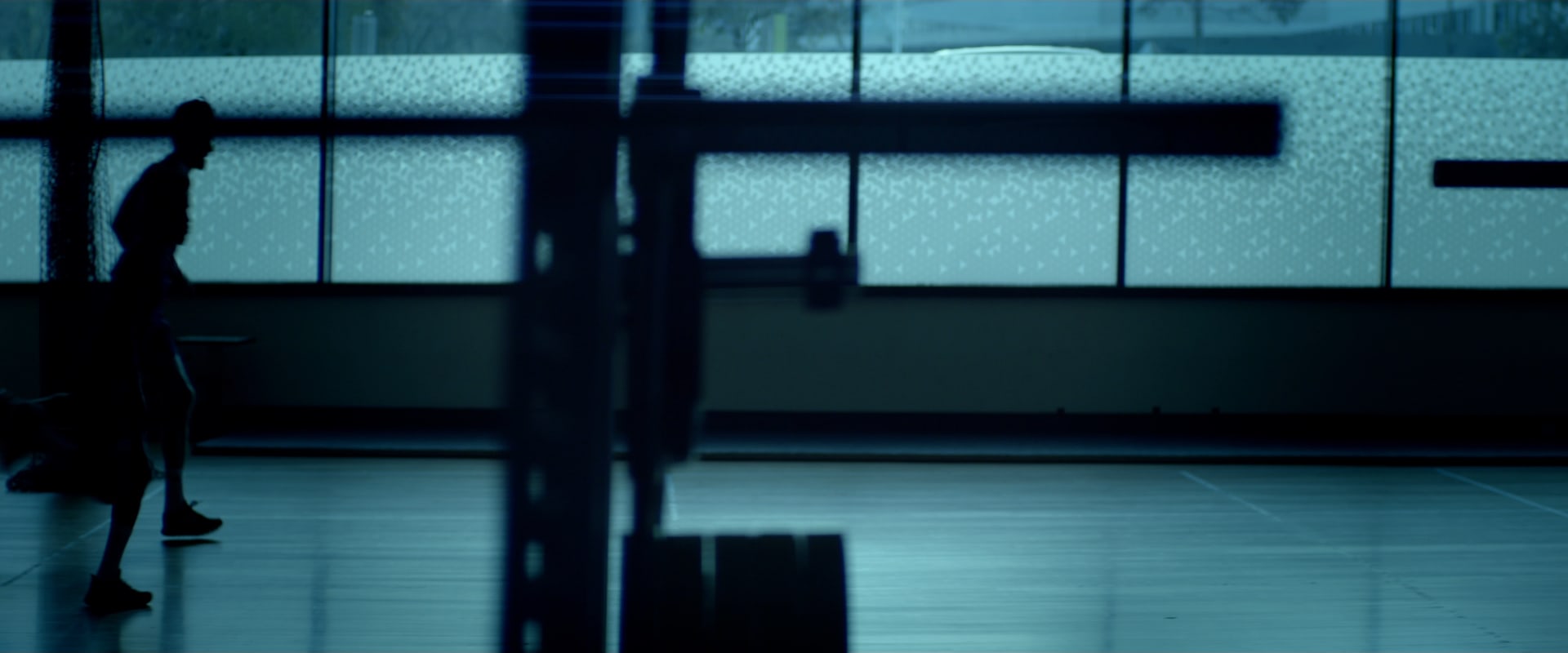 Two players silhouetted, running laps past the tall windows of a training gym.