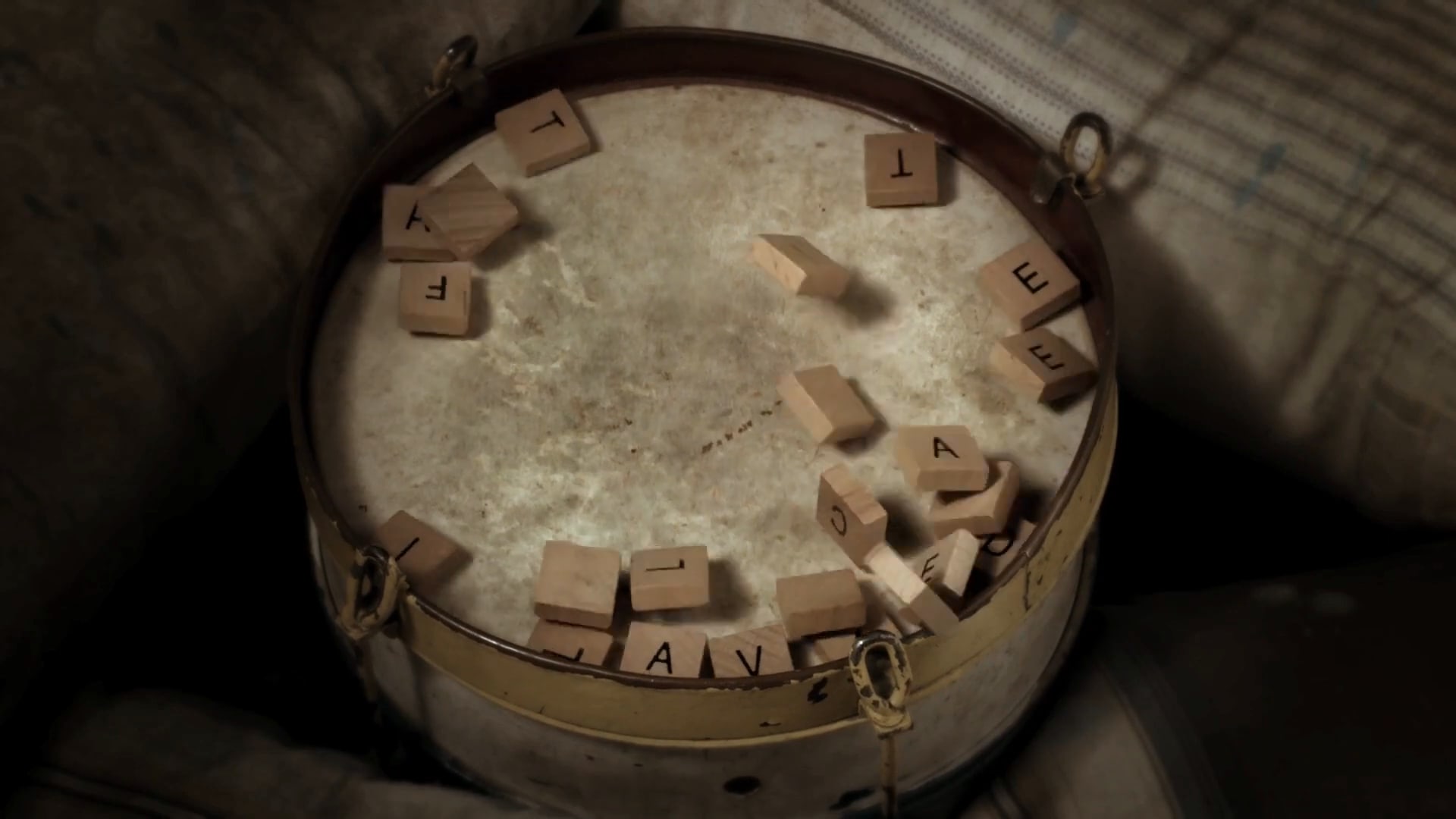 Wooden letter tiles scattered across the skin of an old drum, mid-way between words.