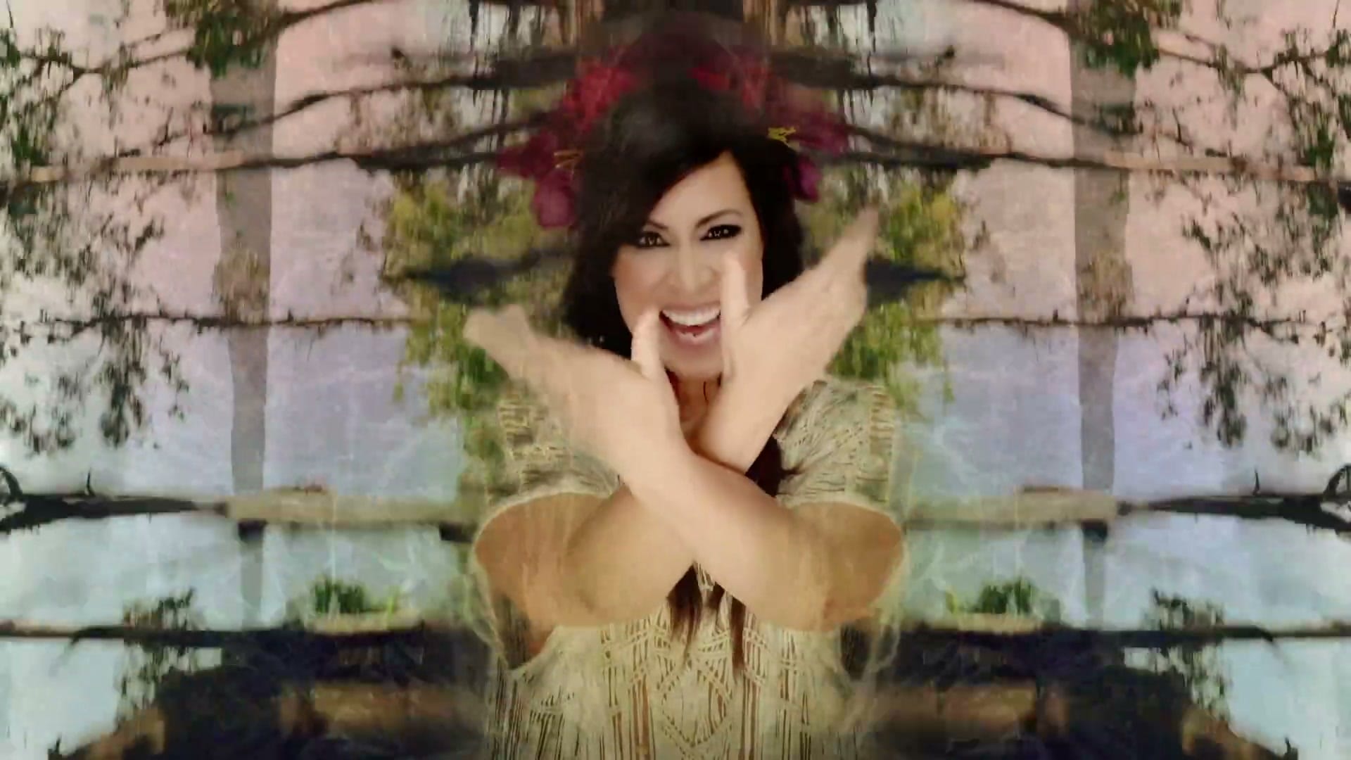 Kate Ceberano laughing with her arms crossed at her chest, flowers in her hair, mirrored gum trees standing either side of her