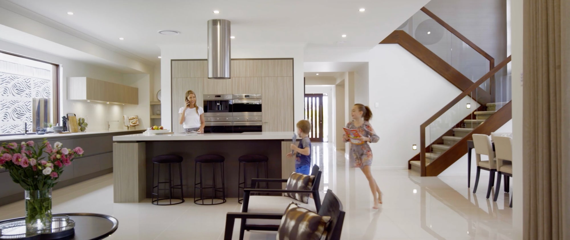 A family kitchen in a Metricon home, a mother at the island bench while two children run across the polished floor.
