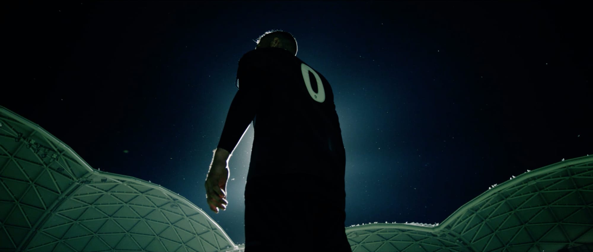 A player walking away in silhouette toward the lit roof of an empty stadium