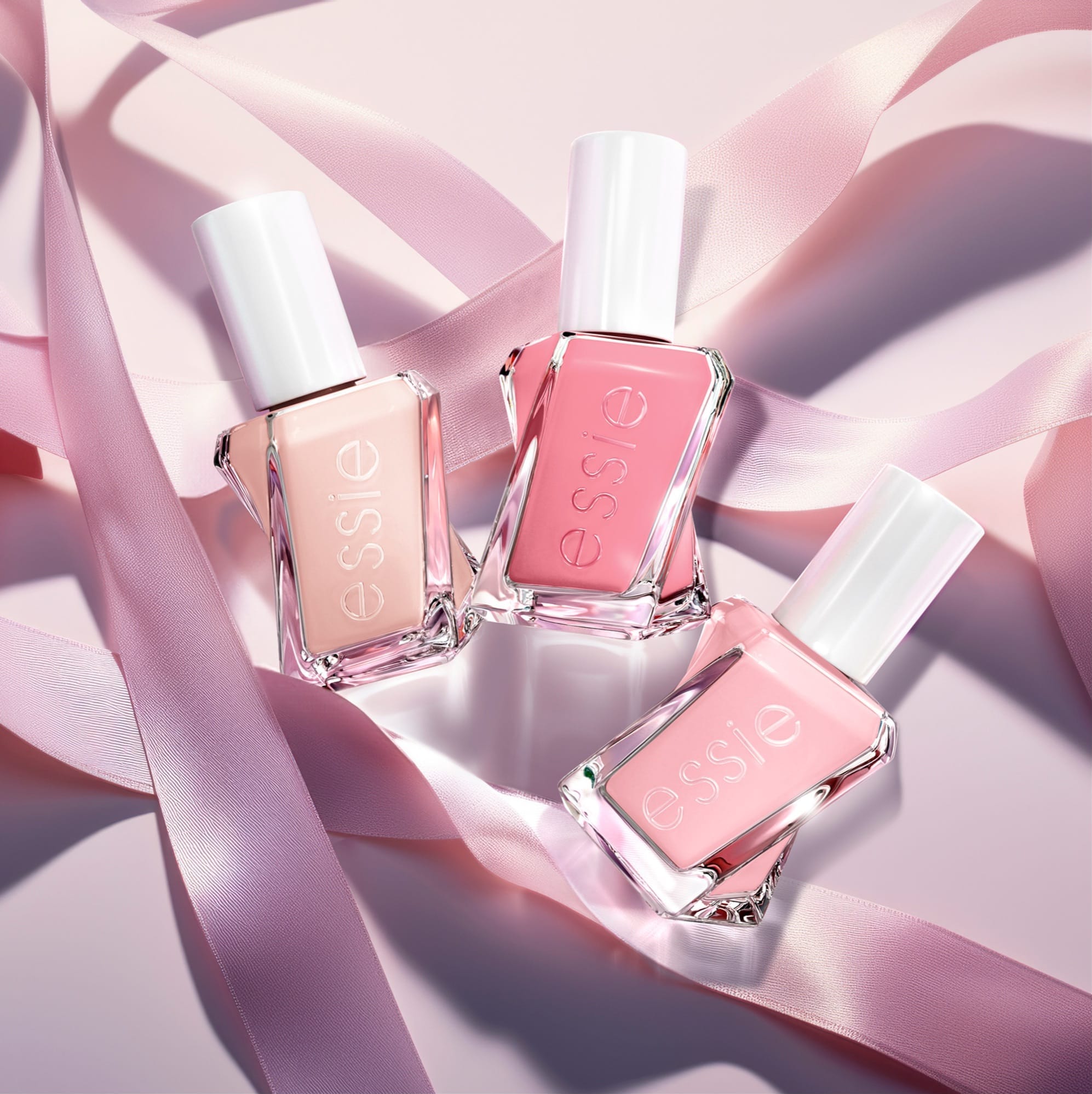 Three sheer nude and pink Essie bottles lying across pale pink silk ribbons.